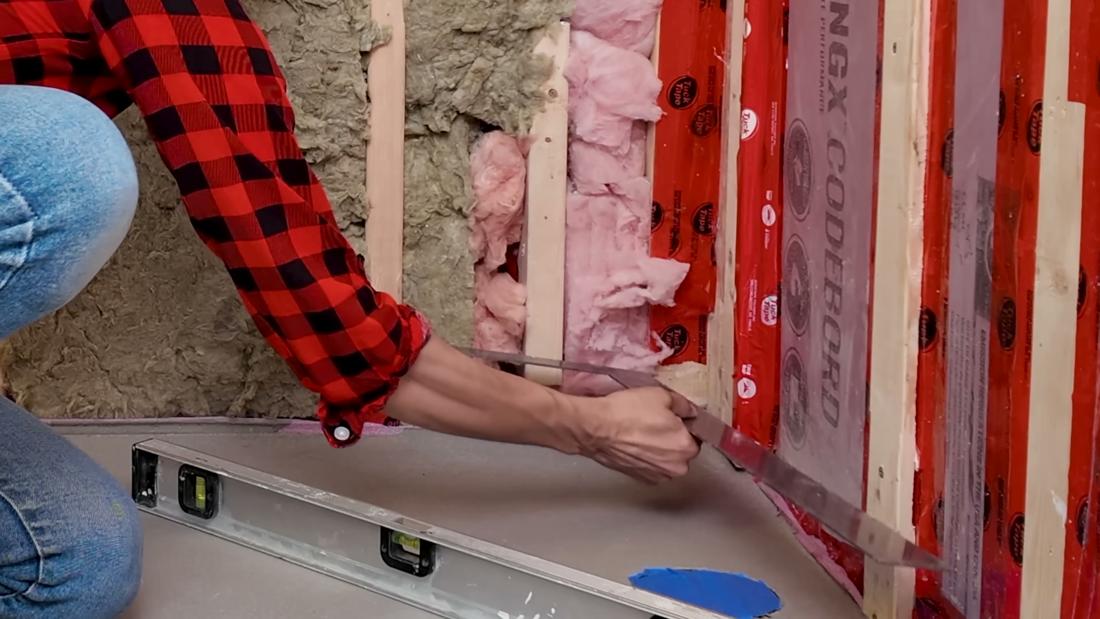 Close-up of a framing square set into a bathroom corner to confirm two shower walls meet at a true 90 degrees