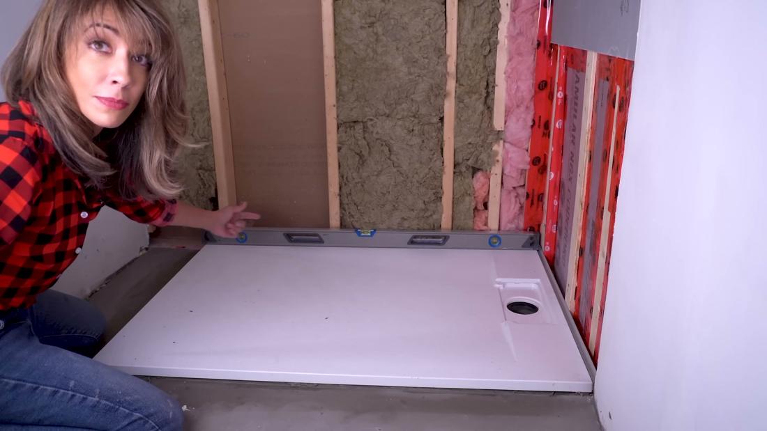 Licensed contractor checking a curbless shower base for level with a long level after setting it in the mortar bed