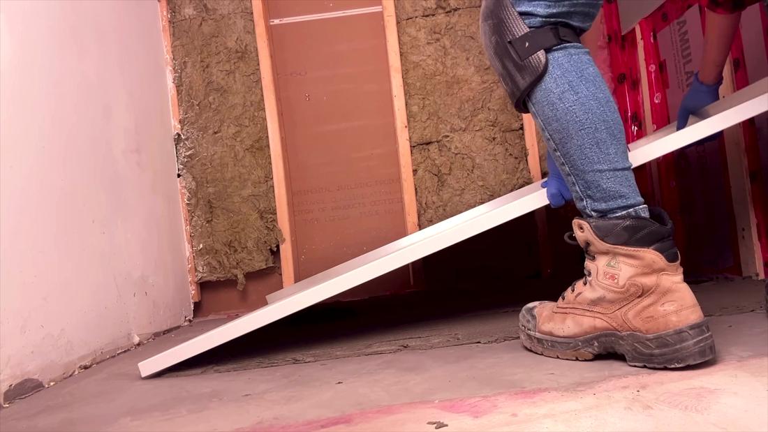 Close-up of a thin solid-surface curbless shower base being carried and lowered into place over the drain, heavier than older vinyl shower bases