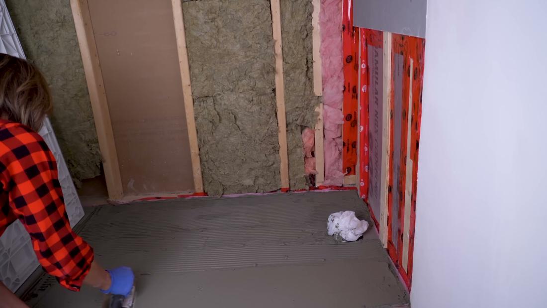Combing thin-set mortar with a half-inch notched trowel to create even ridges before setting the shower base