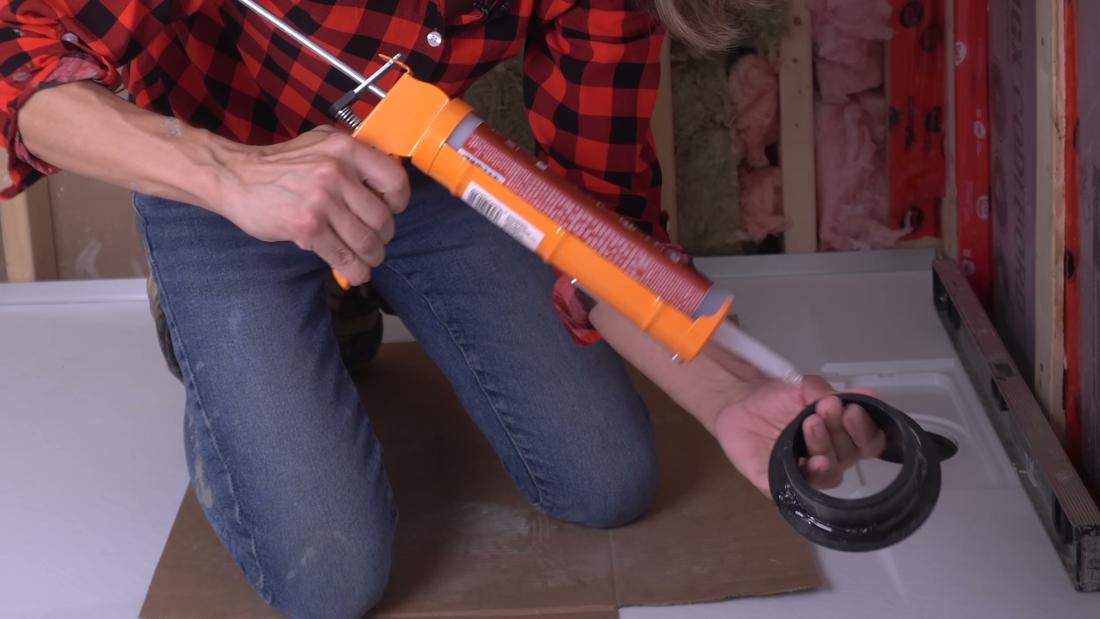 Applying 100% silicone to the backside of a shower drain to prevent leaks and bond it to the curbless base