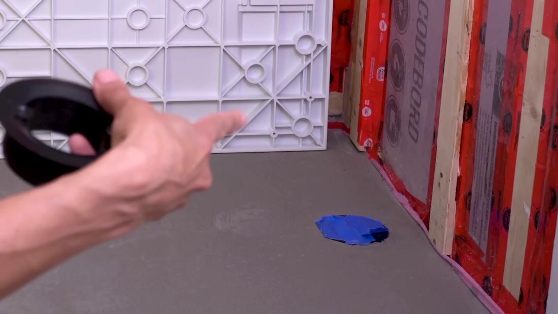 Blue painters tape covering a floor drain rough-in opening to stop debris falling in while working above it