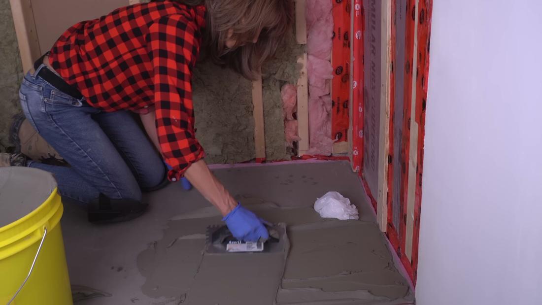 Keying thin-set mortar into the subfloor with the flat side of a trowel, spreading right to left for a curbless shower base