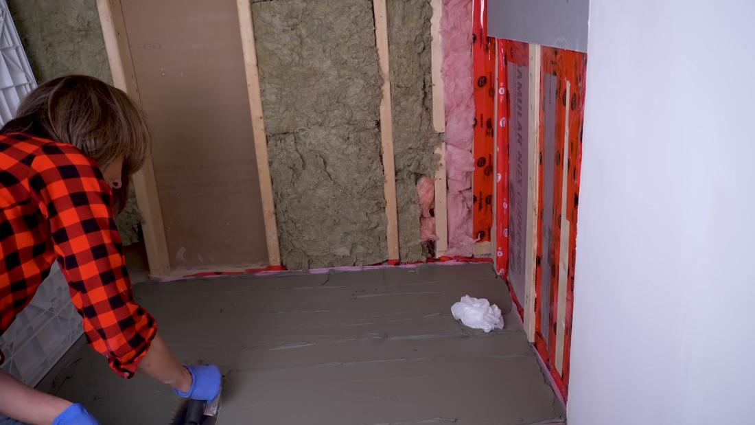 Smoothing thin-set mortar evenly across the whole subfloor before combing it for a curbless shower base